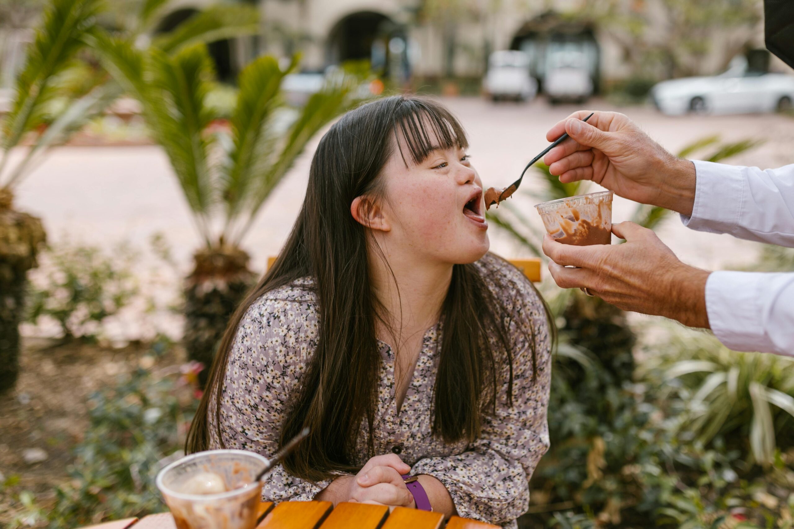 A young woman with Down syndrome enjoys ice cream outdoors with assistance.